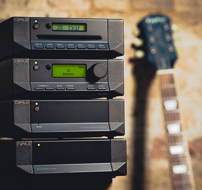 Cyrus CD T CD Transport stacked with other Cyrus products and a guitar leaning beside.