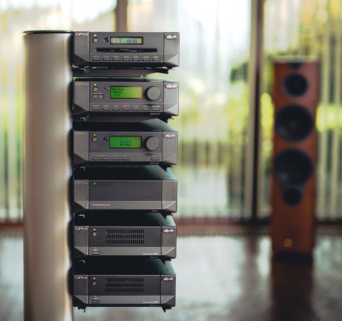 Cyrus Mono X 300 mono power amplifier with other pieces of Cyrus equipment on a stand with a speaker in the background to the right.