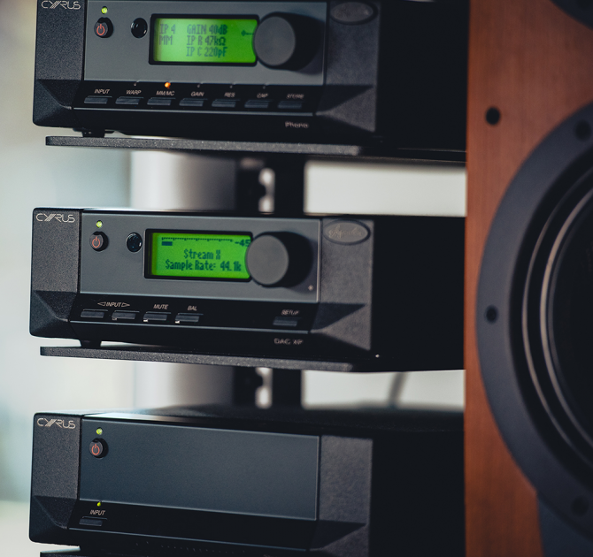 Cyrus Stereo 200 Power Amplifier on a stand with two other pieces of Cyrus equipment and partial view of a speaker to the right.