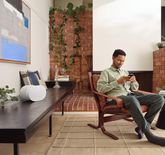 SONOS Era 300 Loudspeaker in white on a long wooden table with a man sitting in a chair.