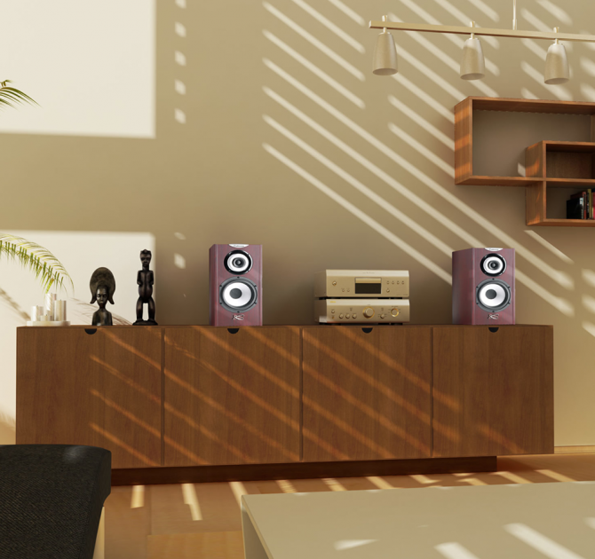 A pair of Cabasse Minorca Loudspeakers with a hifi between on a sideboard with black statues.  There's a large painting on the wall and wooden shelves on the wall.  There's a table in the foreground with two black sofas