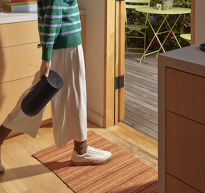 A woman carrying the SONOS Move 2 Loudspeaker in black from inside to outside