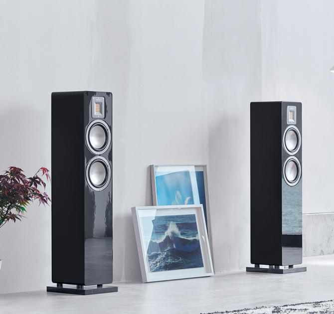 Audiovector QR3 pair in piano black in front of a plain white wall with two pictures in between them leaning against the wall