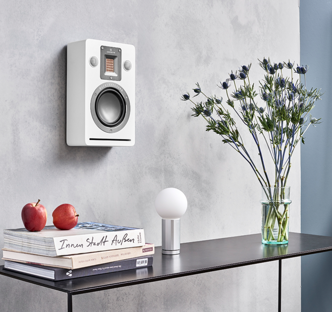 Audiovector QR Wall in white silk above a table with books, a lamp and a vase of flowers on.