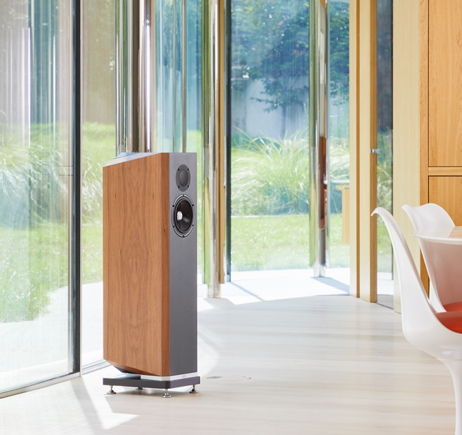 A single Kudos Titan 606 speaker with grill off in a large modern living room in front of glass doors that open onto a garden.