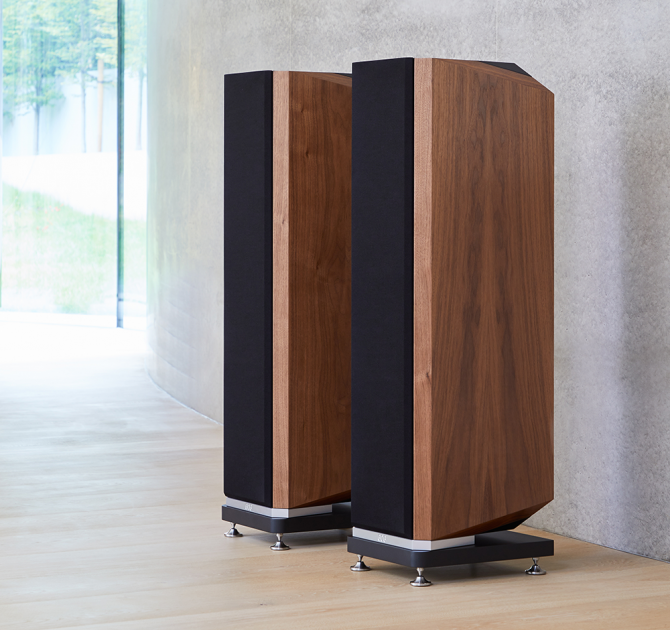 A pair of Kudos Titan 606 speakers with grills on in front of a polished concrete wall.
