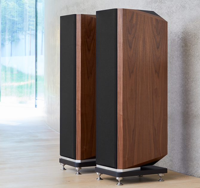 A pair of Kudos Titan 707 speakers with grills on in front of a polished concrete wall.