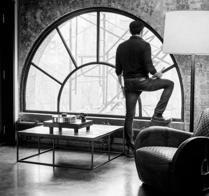 Project Xtension 10 (no cartridge) - Turntable on a low wooden table in front of a large semi-circular window with a man standing and looking out of the window.
