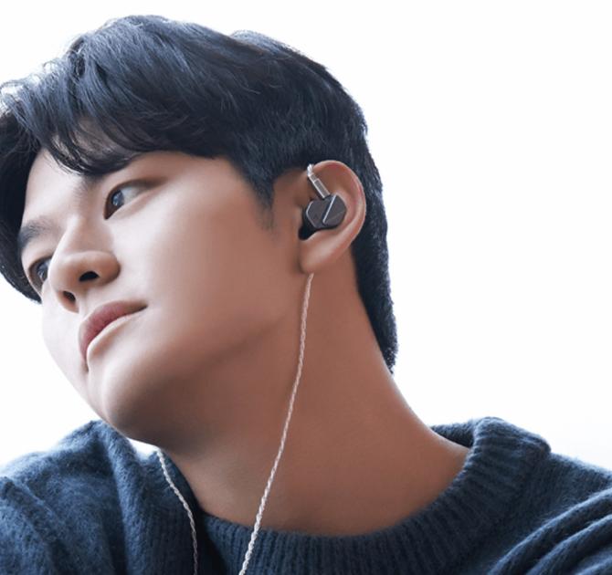 Astell & Kern Zero 2 Earphones in a young man's ears.  He's looking thoughfully to the side and is wearing a dark jumper with stripes