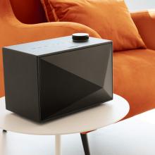 A black Astell & Kern ACRO BE100 Home Audio-Speaker on a small table beside an orange chair