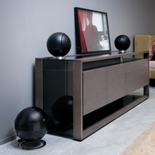 Cabasse Baltic 5 Sub System (on base) in black.  The sub is on the floor.  The Baltic 5s are on a wooden sideboard.  There's a sofa in the background.