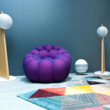 Cabasse Baltic 5 Sub System (on stand).  The sub is white.  the Baltic 5s are white with wooden stands.  There's a geometric rug on the floor.  The wall is painted dark grey and there's a purple chair that looks like a solid beanbag.