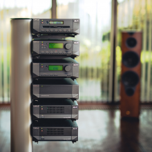 Cyrus Mono X 300 mono power amplifier with other pieces of Cyrus equipment on a stand with a speaker in the background to the right.