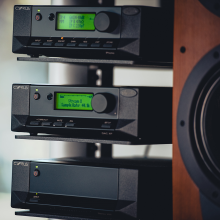 Cyrus Stereo 200 Power Amplifier on a stand with two other pieces of Cyrus equipment and partial view of a speaker to the right.