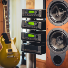 Cyrus Stereo 200 Power Amplifier on a stand with other pieces of Cyrus equipment with a speaker to the right and a guitar to the left.