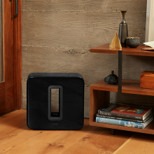 SONOS Sub in black next to a set of floor standing shelves
