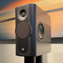 a grey rectangular speaker on a black stand with a piece of artwork in the background.