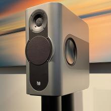 A rectangular speaker on a stand with a piece of art on the wall in the background.