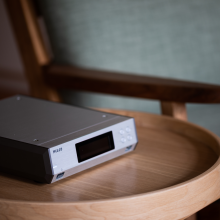 Melco N100 - HiRes Music Library.  Pictured on a wooden, circular table with a chair in the background.