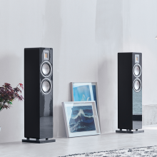Audiovector QR3 pair in piano black in front of a plain white wall with two pictures in between them leaning against the wall