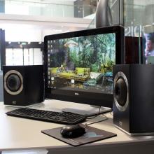 A pair of Cabasse Rialto Loudspeakers in black either side of a computer screen with a keyboard on the desk too.