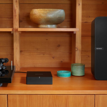 SONOS Port on a wooden sideboard with a bowl on a shelf above it and a SONOS Play:5 to the right.