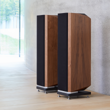 A pair of Kudos Titan 606 speakers with grills on in front of a polished concrete wall.