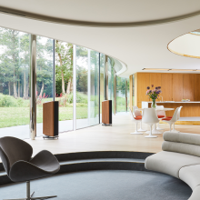 A pair of Kudos Titan 606 speakers with grill on in a large open plan living room in front of glass doors that open onto a garden.