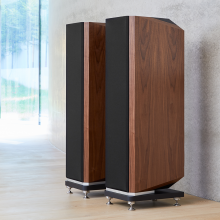 A pair of Kudos Titan 707 speakers with grills on in front of a polished concrete wall.