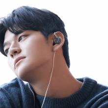 Astell & Kern Zero 2 Earphones in a young man's ears.  He's looking thoughfully to the side and is wearing a dark jumper with stripes